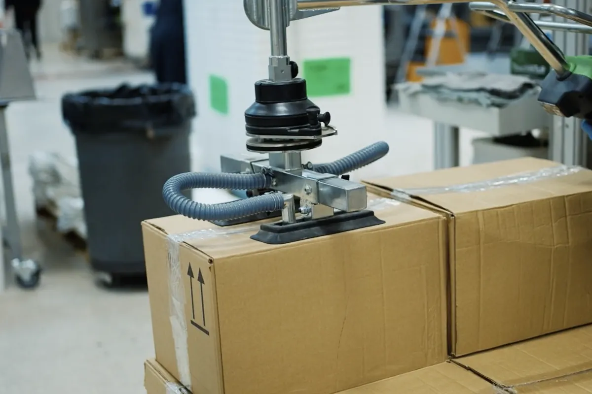 Opérateur déplaçant des cartons avec un manipulateur à ventouse sur la ligne de production